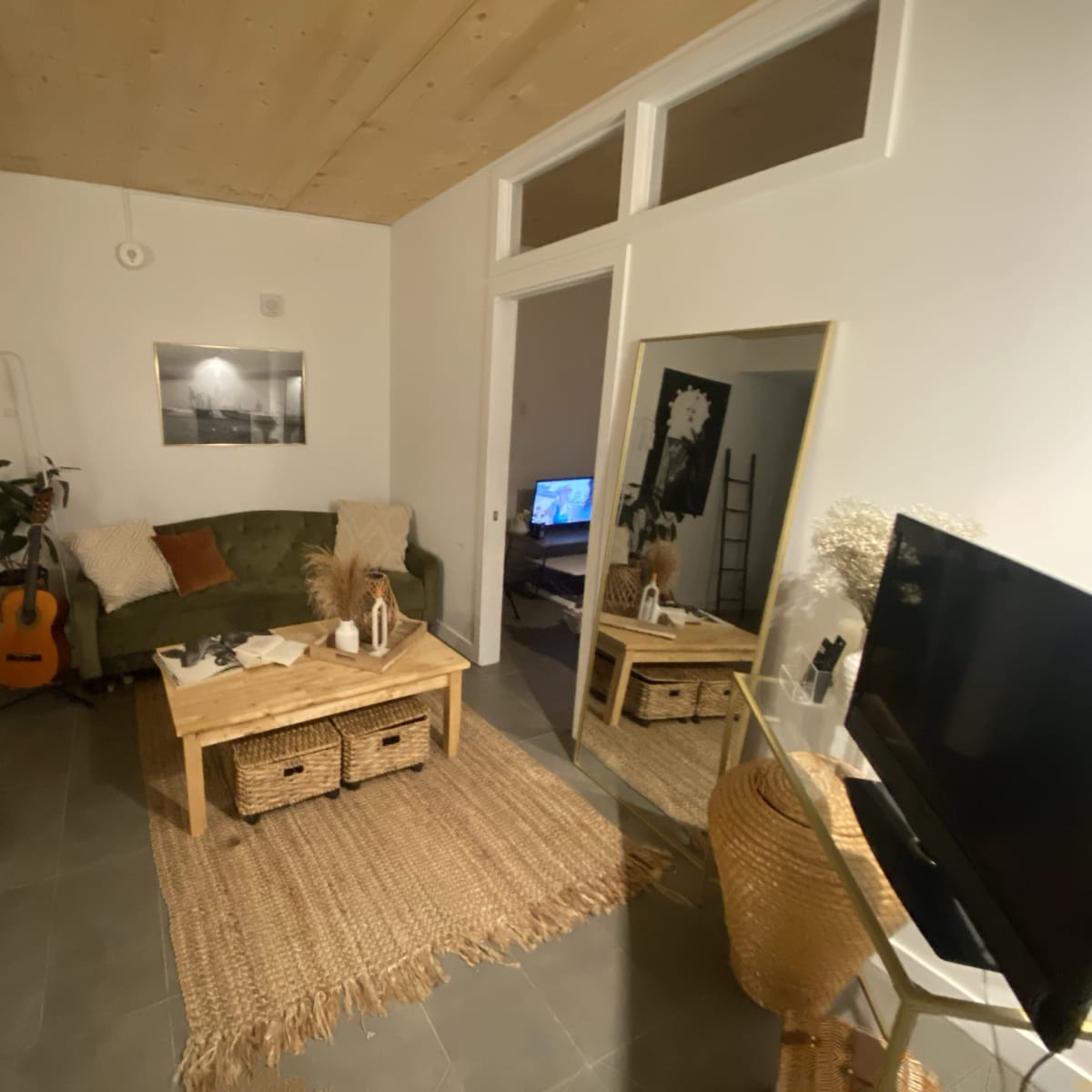 A modern living room with a green sofa, a wooden coffee table, a large mirror, and a television, surrounded by various decorative elements.