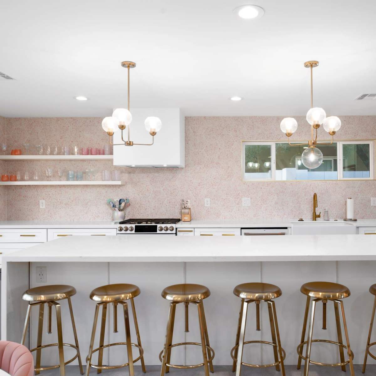 A modern kitchen featuring a large island with gold bar stools, white cabinetry, and decorative lighting fixtures.