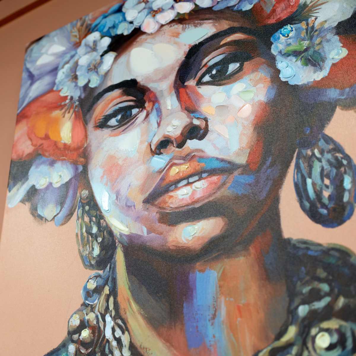 A colorful portrait of a woman adorned with flowers and intricate earrings mounted on a peach-colored wall.