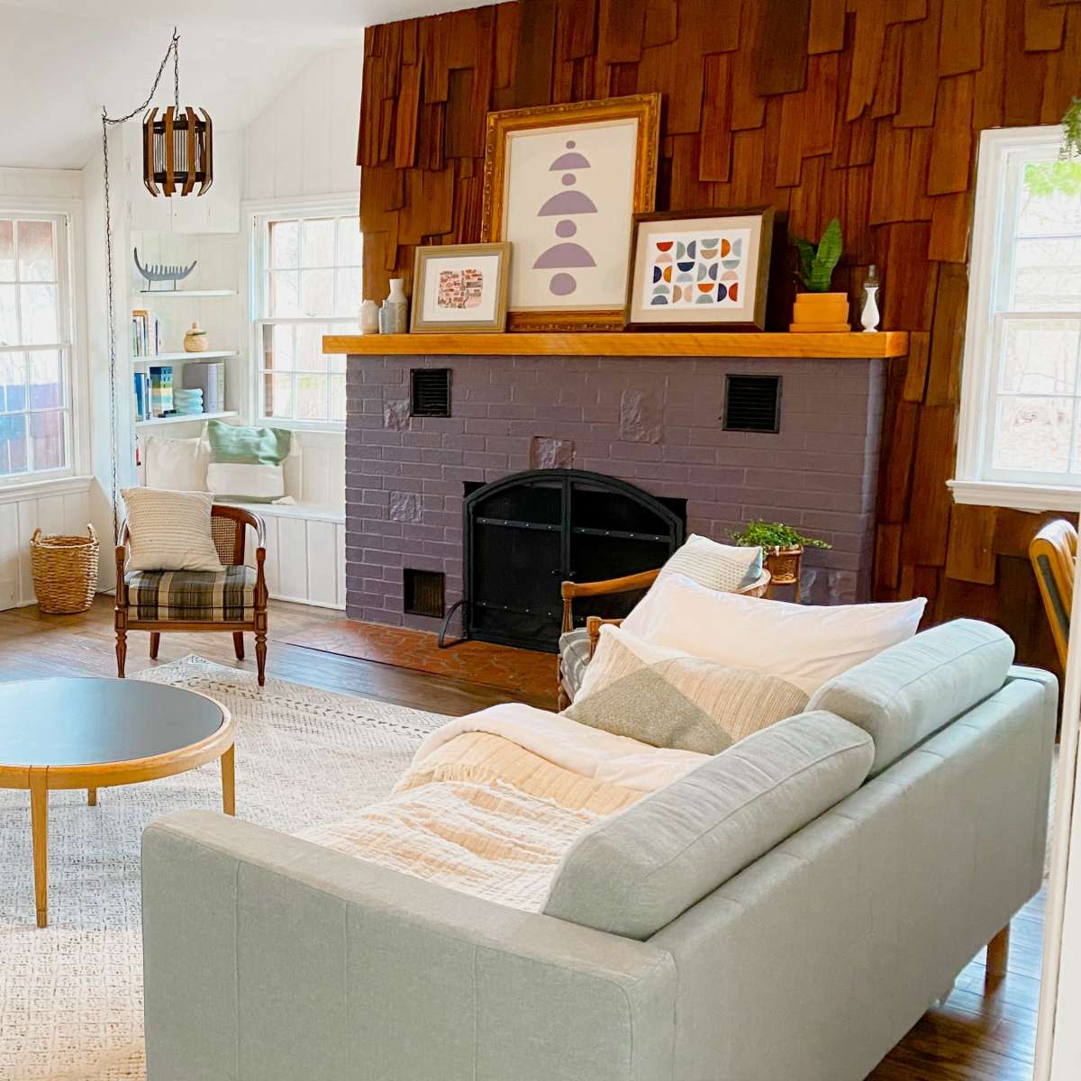 A cozy living room with two light gray sofas facing a round coffee table, a television on one wall, and a fireplace with wood paneling on the opposite wall.