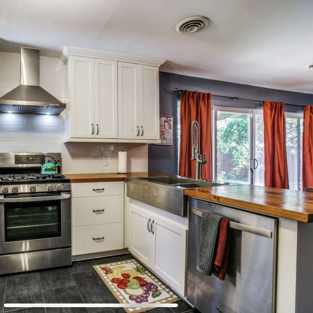 The kitchen features white cabinetry, a stainless steel stove and hood, and a large farmhouse sink with a wooden countertop.