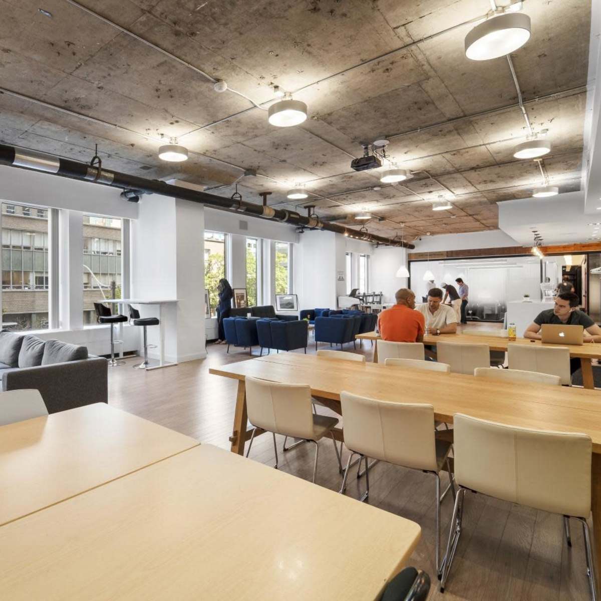 A spacious modern office with tables, a gray sofa, and people working in various activities.