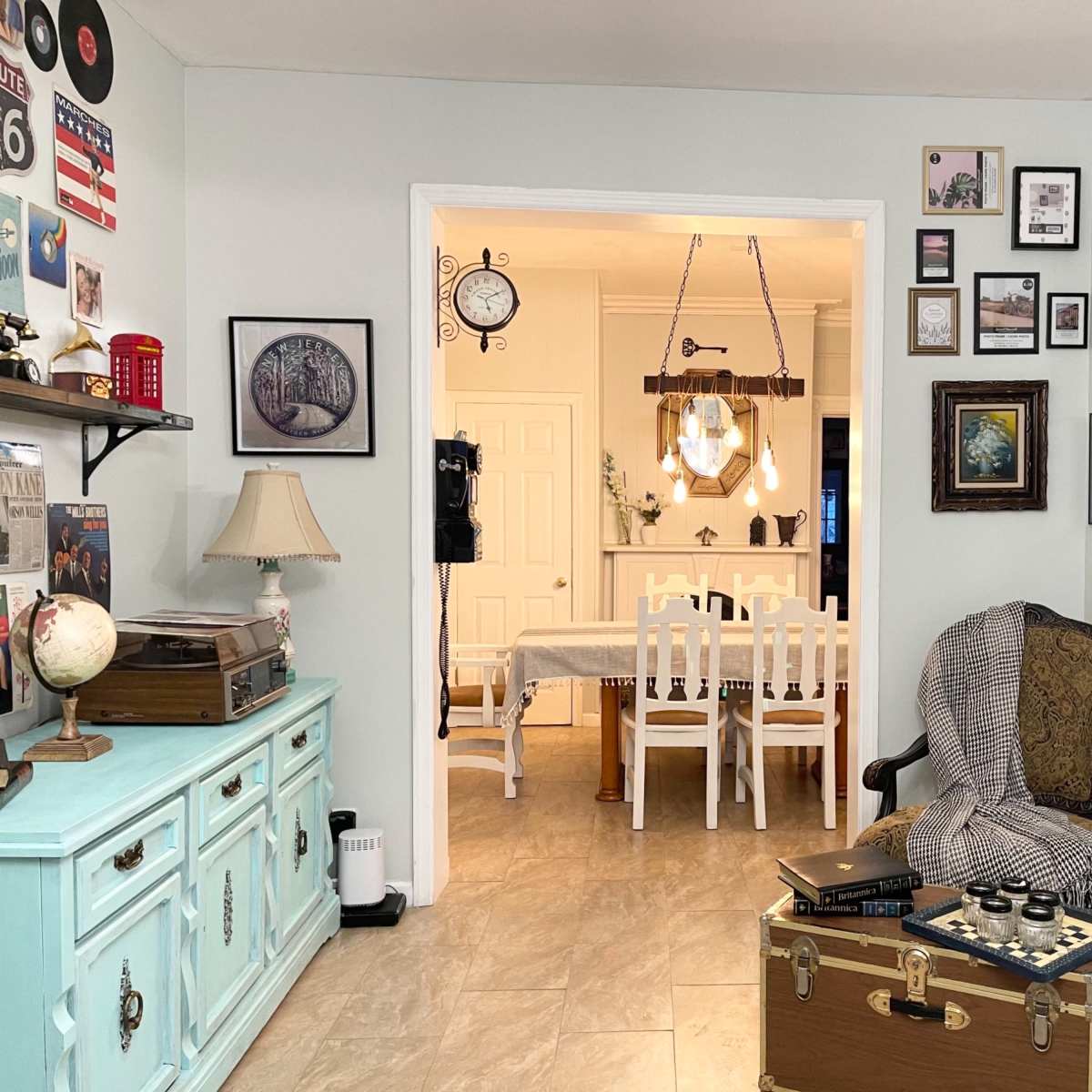 A cozy, decorated living space features a sitting area with a chair and trunk, leading to a dining area furnished with a table and chairs.