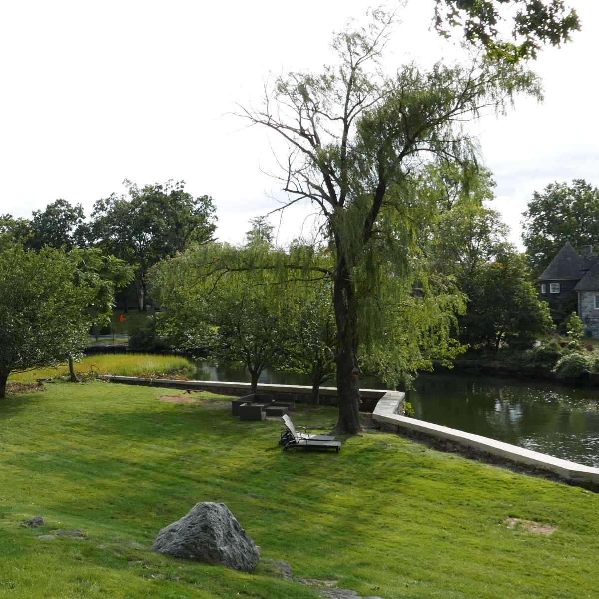 A grassy area features trees and a small pond in the background, with a stone and a bench positioned nearby.
