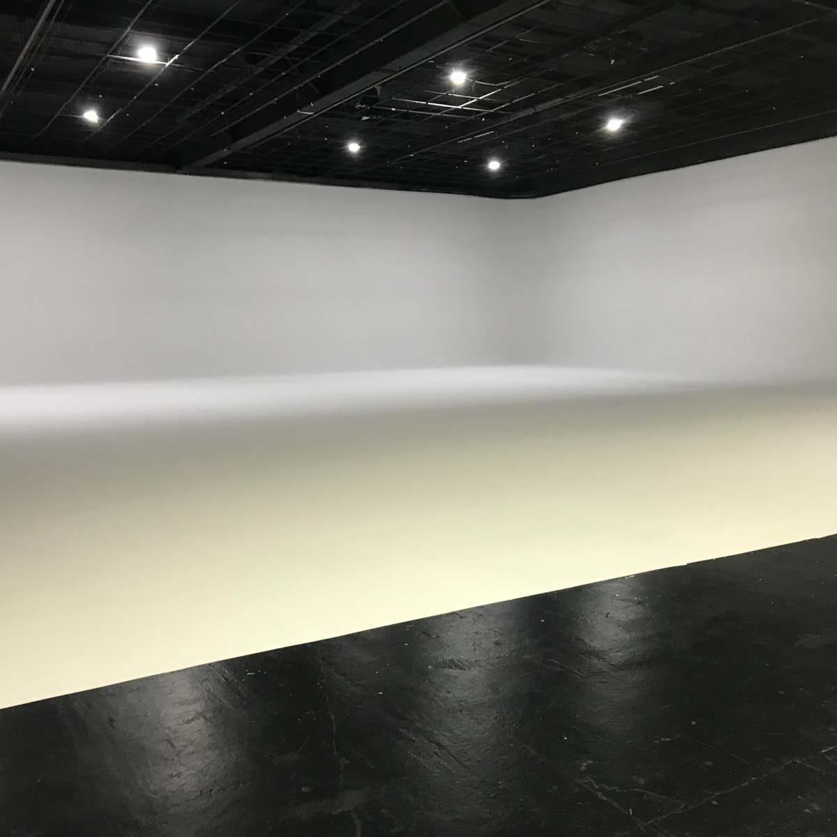 A large empty studio space with a seamless white backdrop and a black floor.