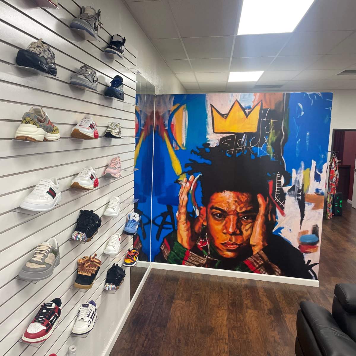 A sneaker shop with various shoe styles displayed on white slat walls and a large mural of a young man in a crown on the adjacent wall.