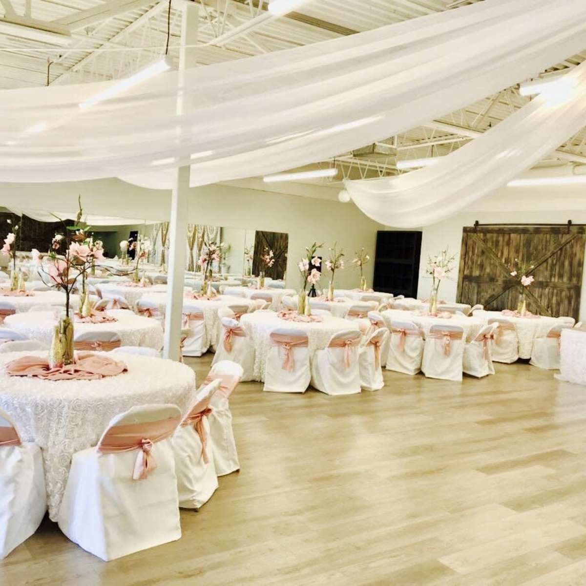 A spacious event hall is set up for a banquet, featuring round tables dressed in white linens with pink sashes and floral centerpieces.