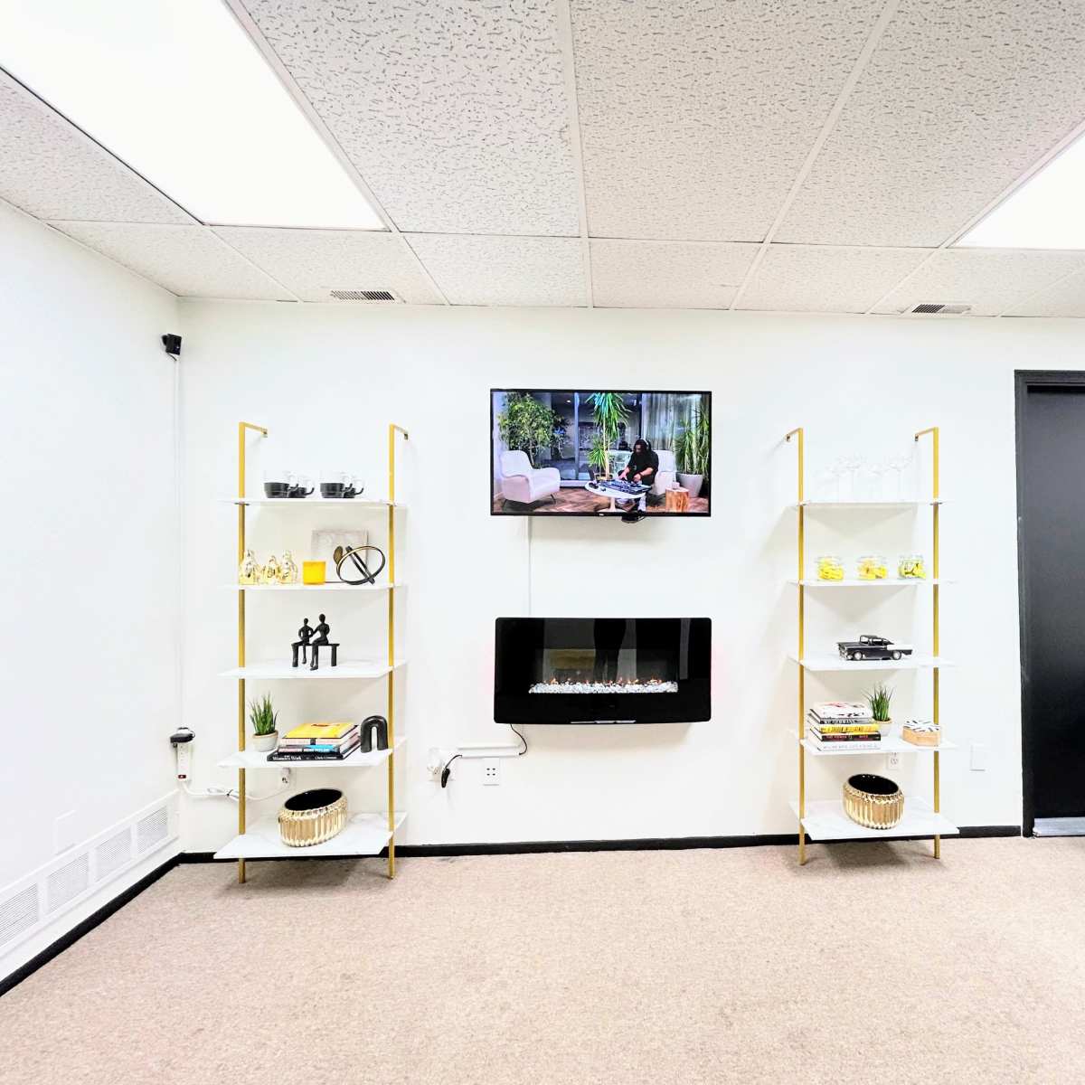 A modern room with two shelving units on either side, a wall-mounted television above an electric fireplace, and a black chair positioned in front.