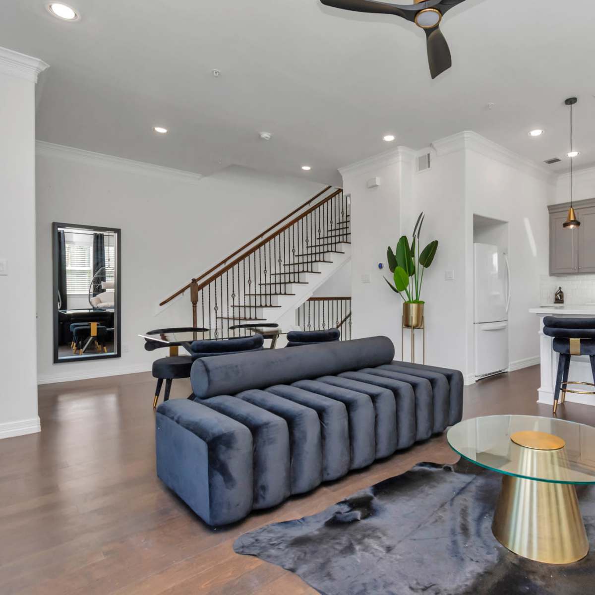 A modern living space featuring a sectional sofa, a glass coffee table on a rug, and a staircase leading to an upper level.