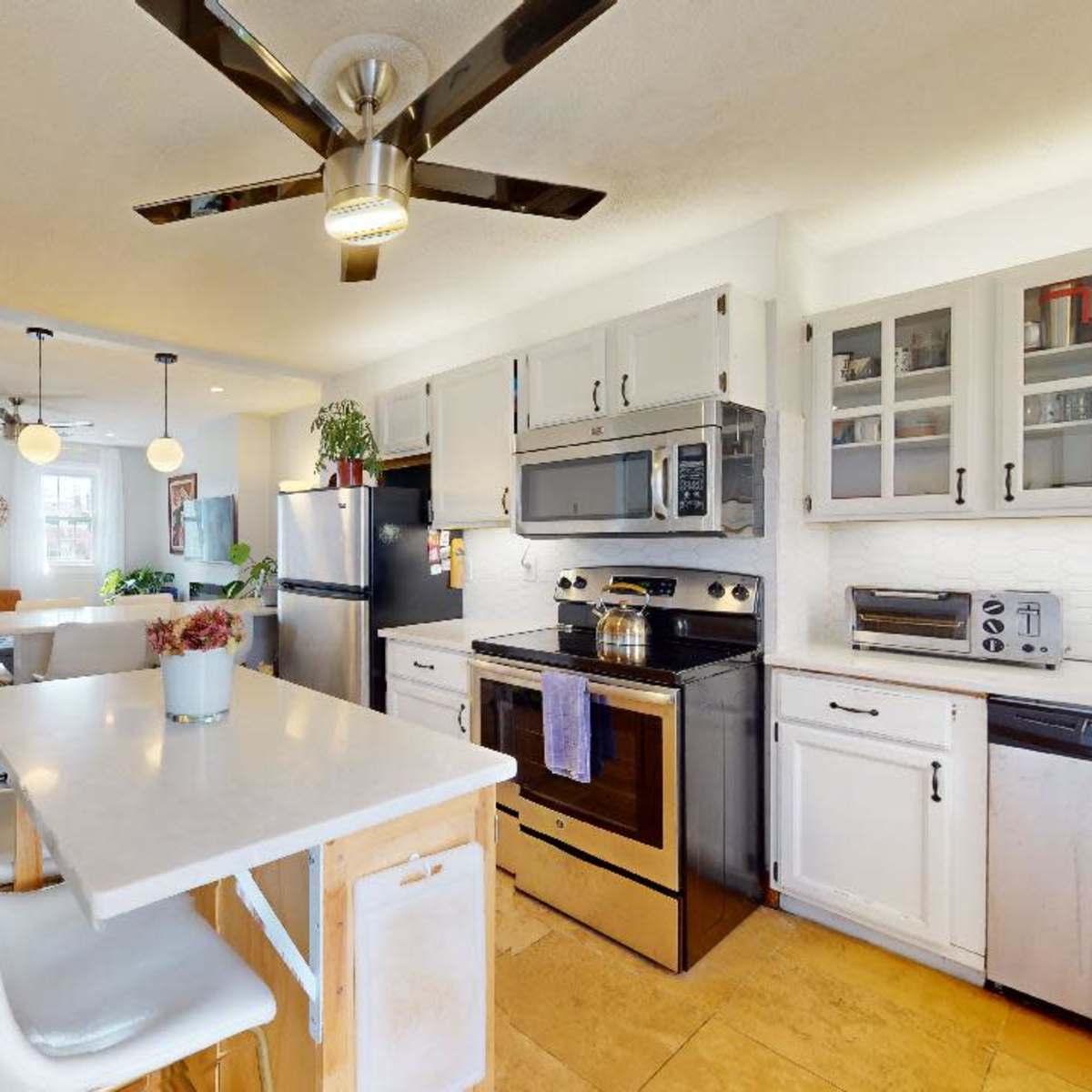 The kitchen features a central island with seating, stainless steel appliances, and white cabinetry that opens to a living area.