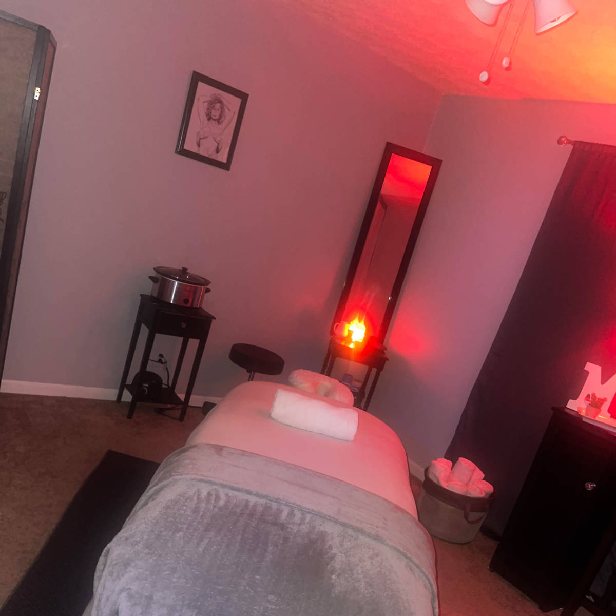 A serene massage room featuring a massage table with a towel, a mirror, a salt lamp, and a cozy seating area.