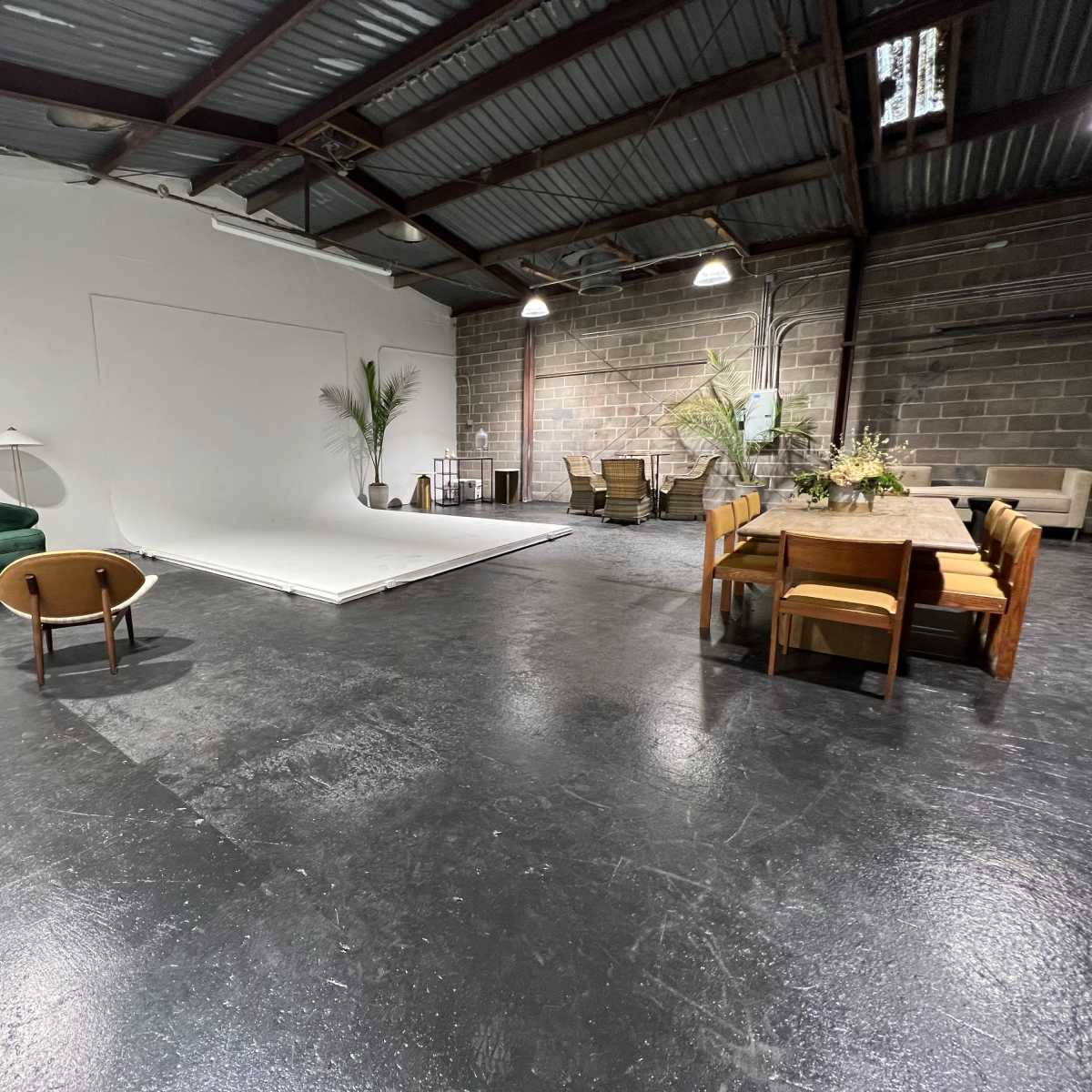 An industrial-style interior space featuring a green sofa, two wooden chairs, a dining table, and a backdrop area.