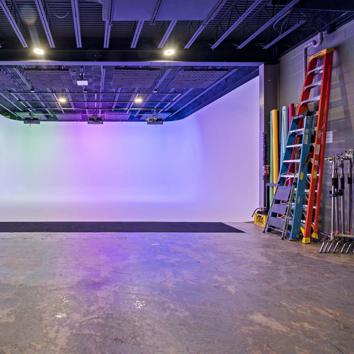 An empty photo studio with a curved backdrop, colorful lighting, and various equipment visible in the background.