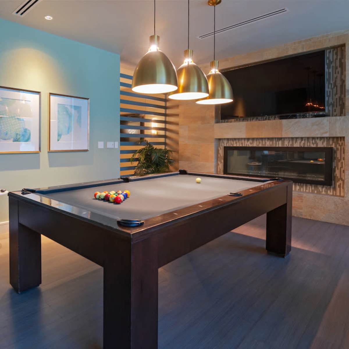 A pool table is centered in a modern game room with decorative walls, pendant lighting, and a fireplace.