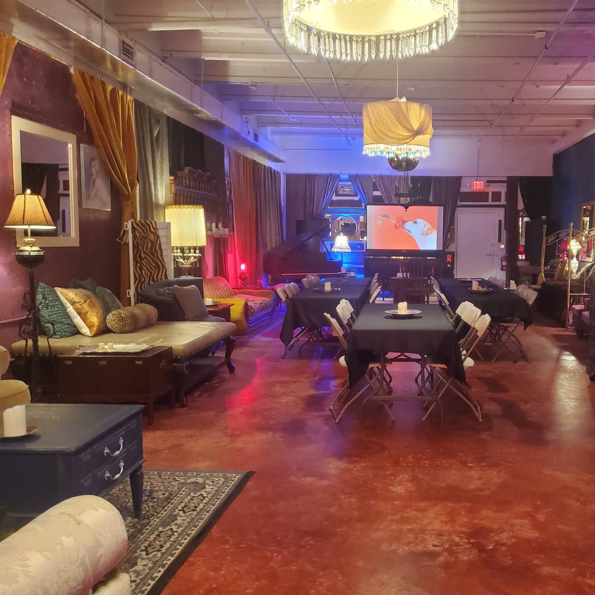 The scene shows a spacious indoor event space with tables set up for dining, comfortable seating areas, and decorative lighting.