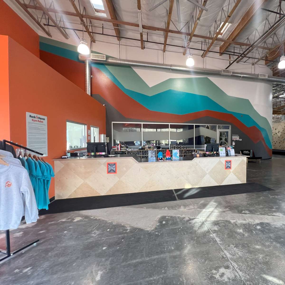 A brightly colored indoor climbing gym with a reception area featuring a geometric wall design and climbing walls in the background.