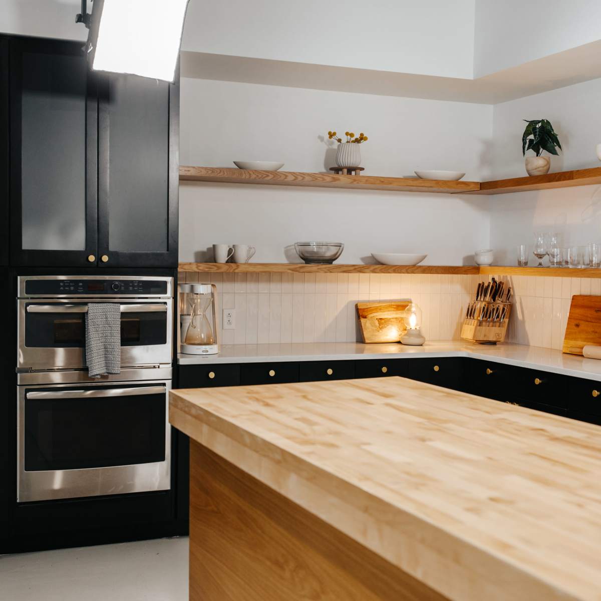 A modern kitchen featuring black cabinetry, stainless steel appliances, and a wooden island.