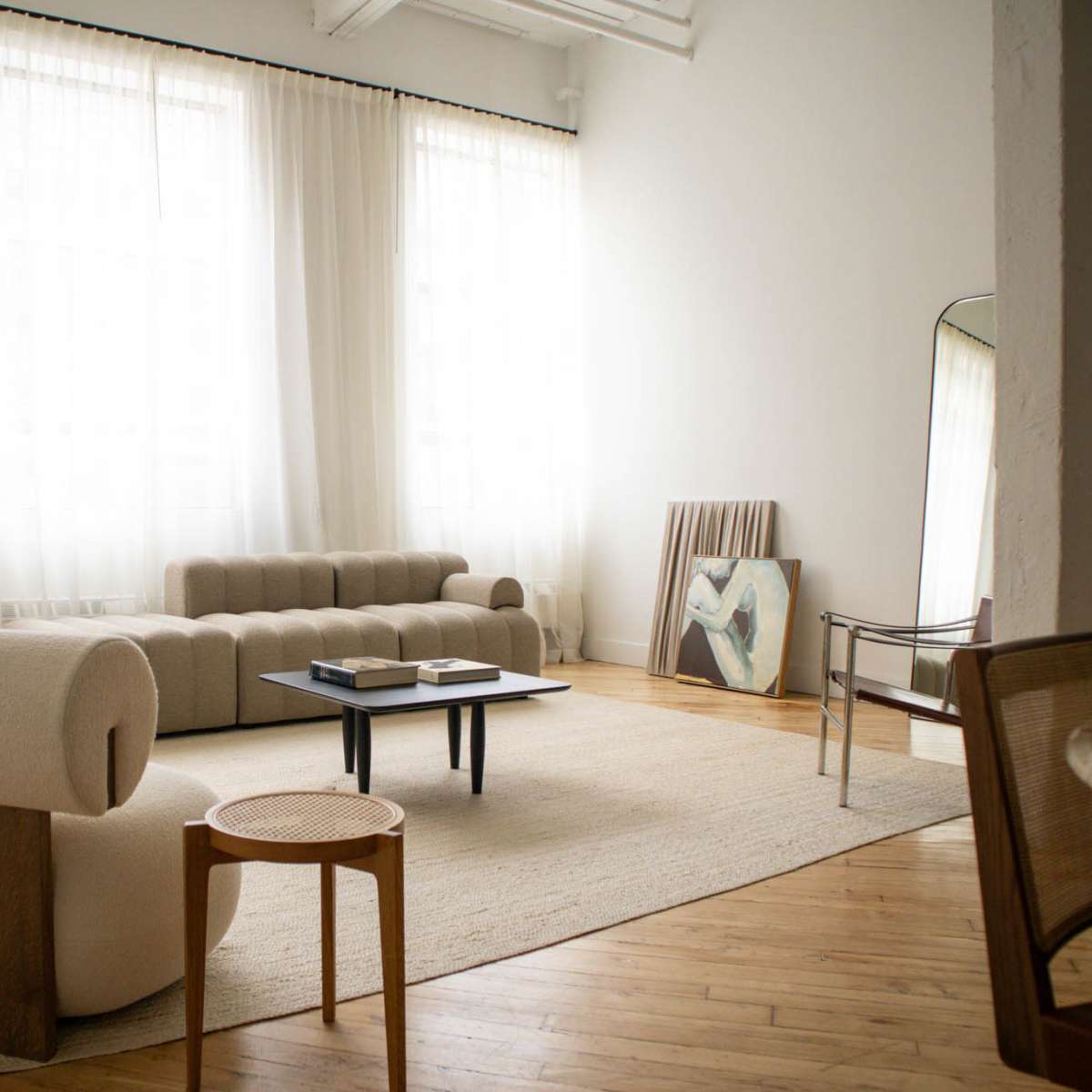 A spacious living room with large windows, two sofas, a coffee table, and a painting leaning against the wall.