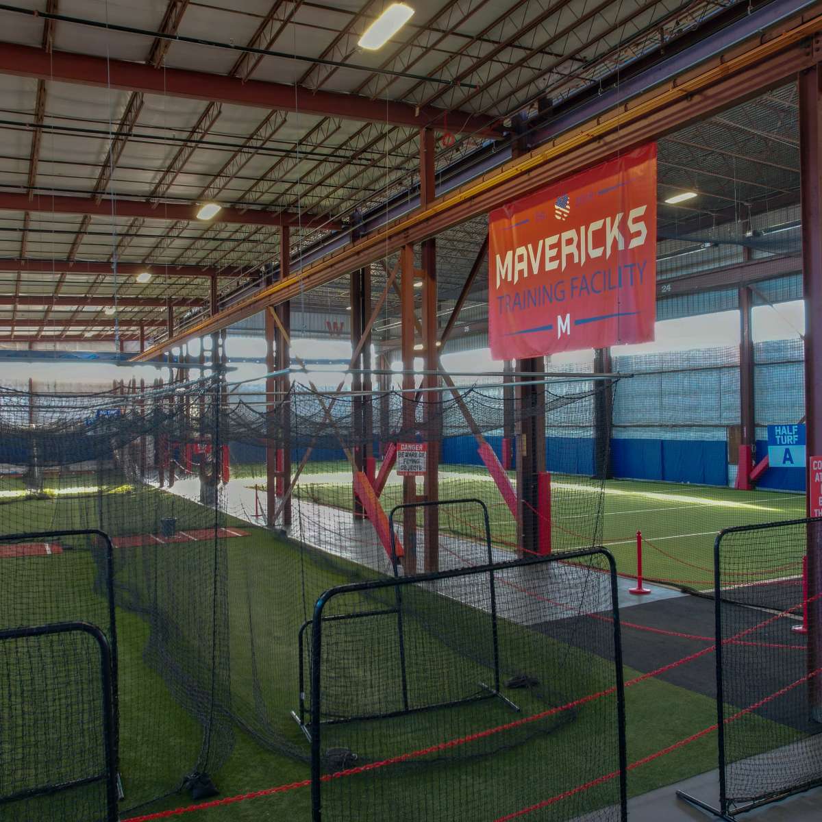 The interior of the Mavericks Training Facility, featuring a turf area surrounded by netting and training equipment.