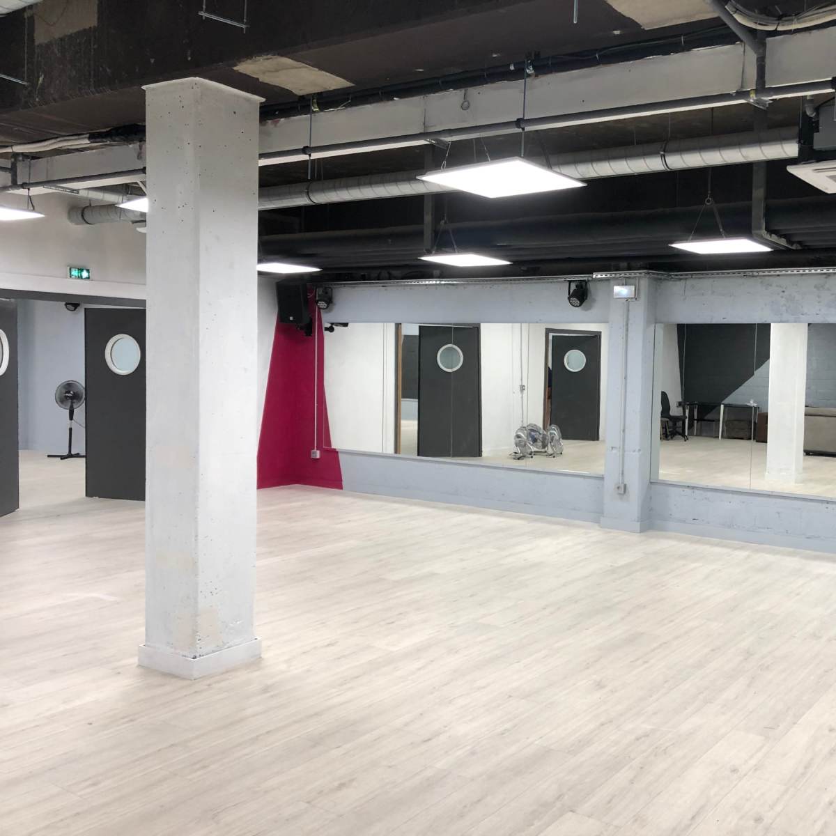 A spacious, empty studio with two large mirrors, gray walls, and separate doors, along with a staircase in the background.