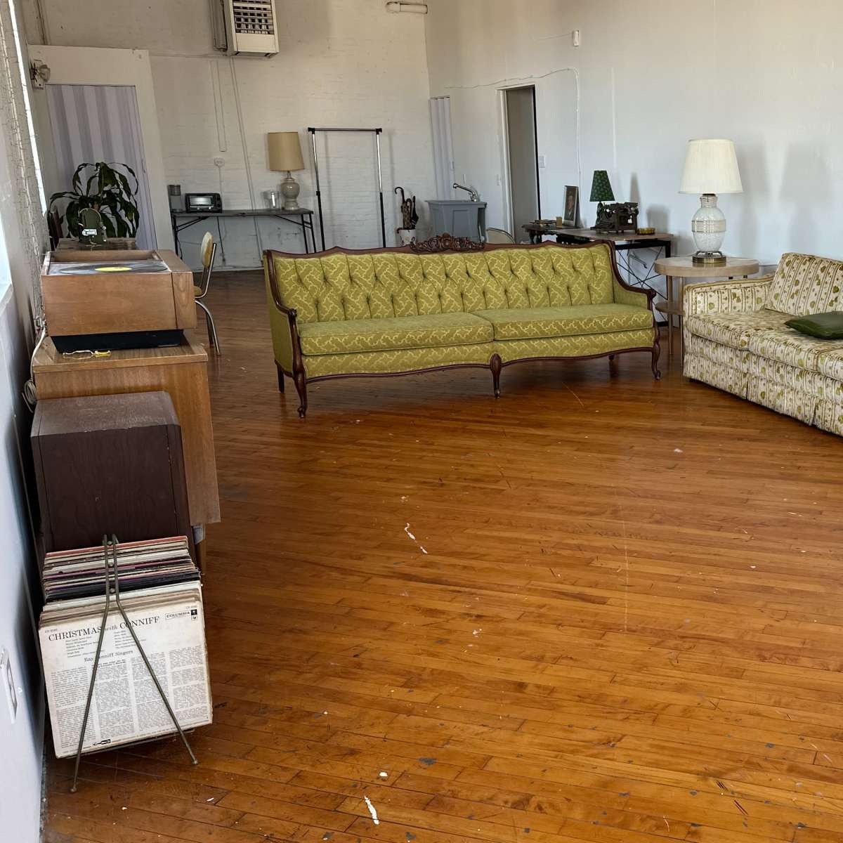 A spacious room with two couches, a side table, and a wooden floor, featuring vintage decor elements.