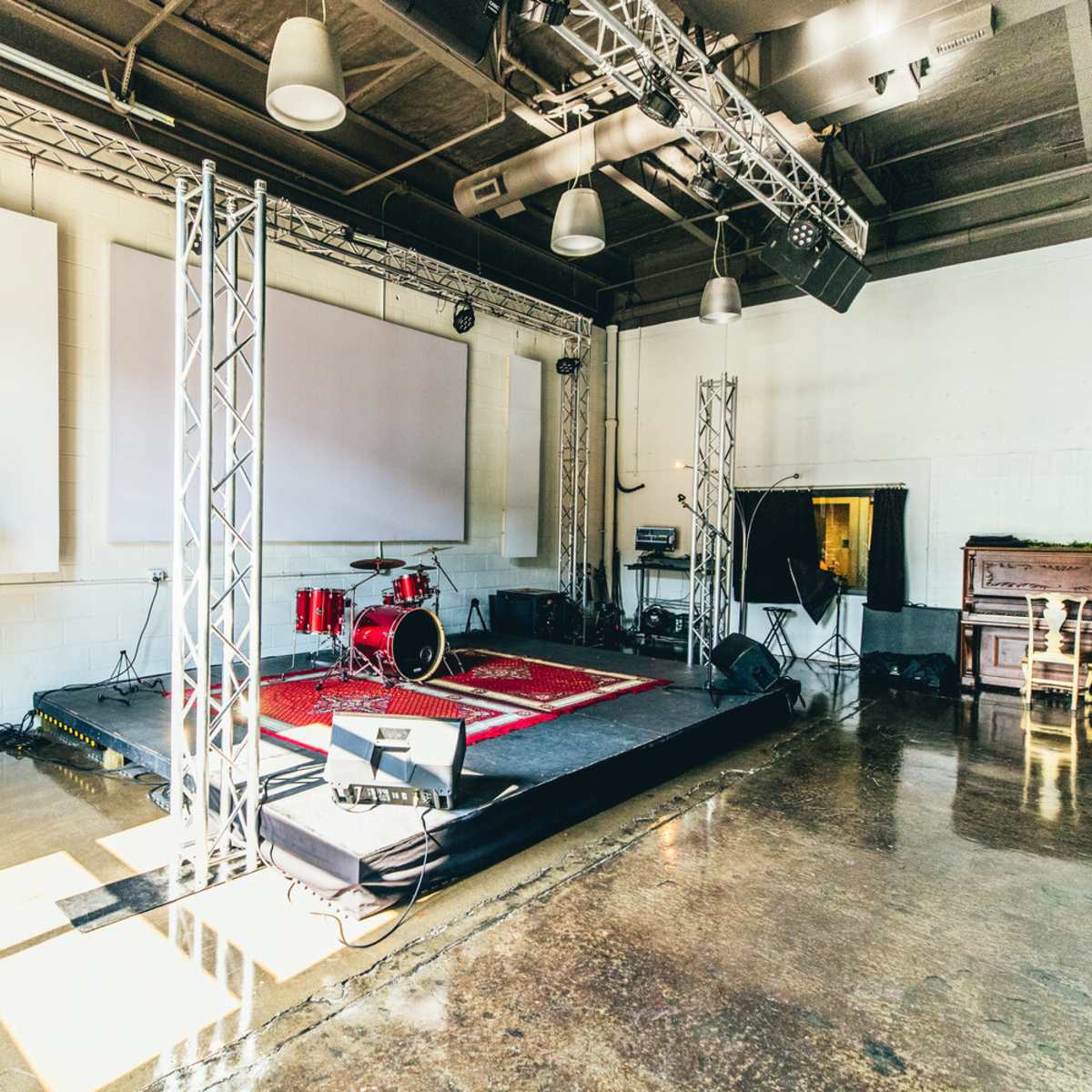 A performance stage featuring a drum set, a piano, and various sound equipment in a spacious, well-lit room.