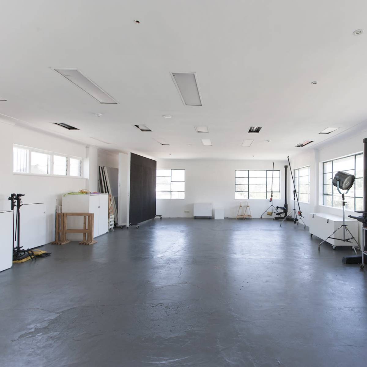 A large, empty studio space with a concrete floor, white walls, and several pieces of furniture and equipment arranged along the periphery.