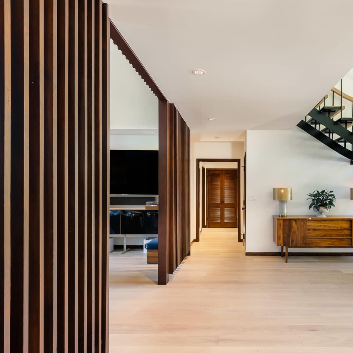 A modern interior featuring a spiral staircase, wooden accents, and a sideboard beside large windows.
