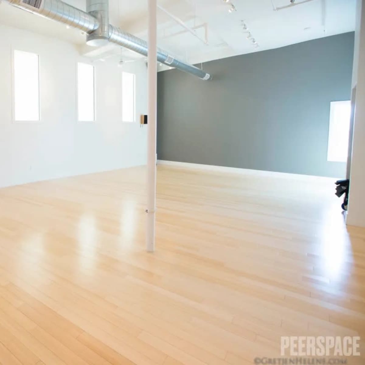 A spacious, minimalist room with hardwood floors, white walls, and a dark gray accent wall.