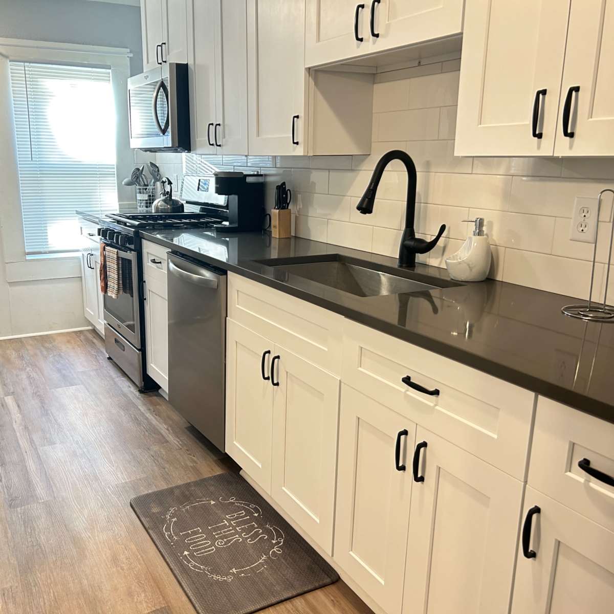 A modern kitchen featuring white cabinets, a stainless steel refrigerator, a black faucet, and a window with natural light illuminating the space.