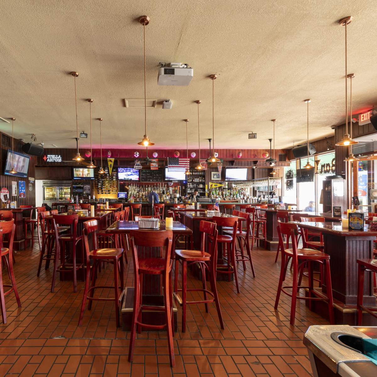 A spacious bar interior with wooden furniture, multiple televisions, and a well-stocked counter.