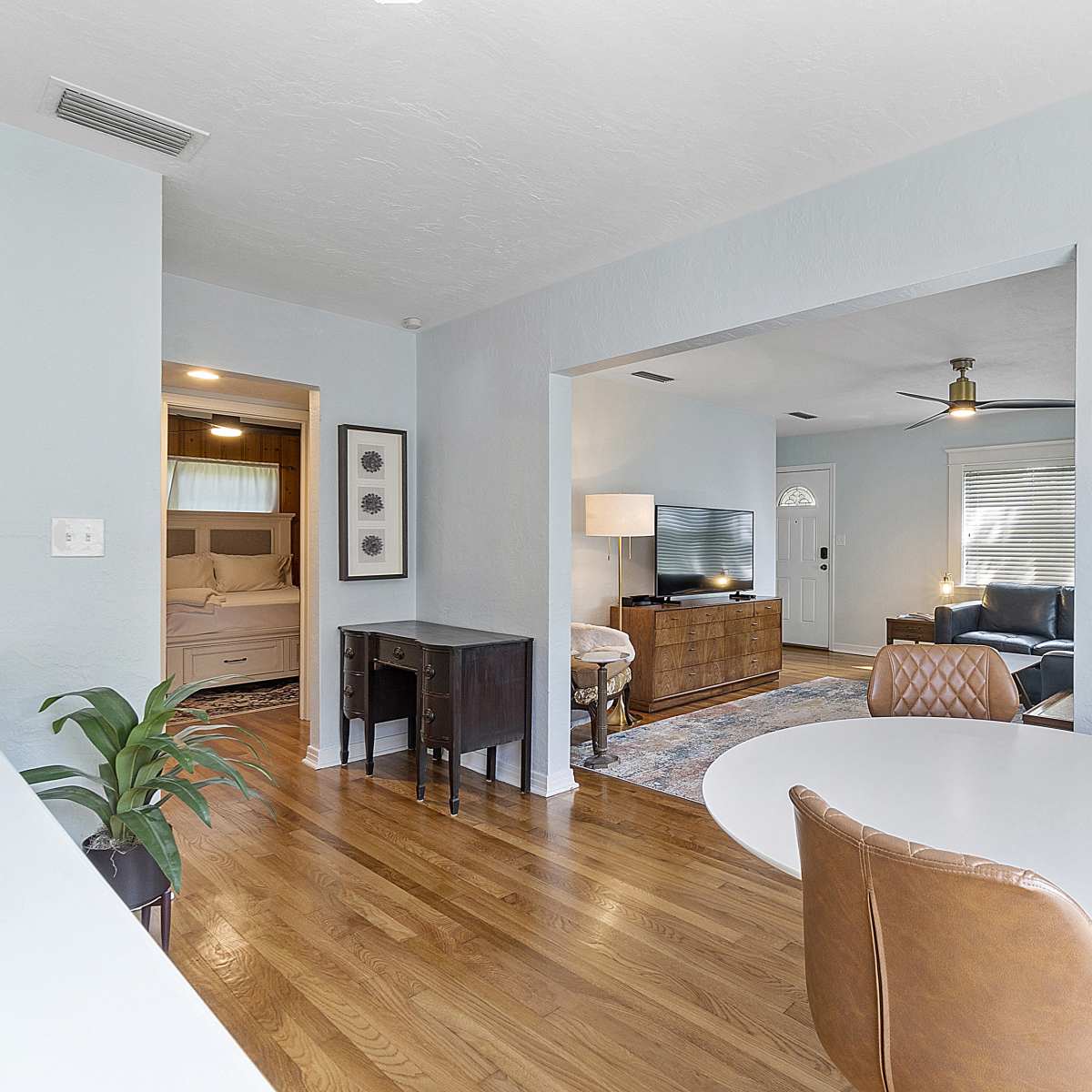 An open living area with hardwood floors, a round dining table, and a view into a bedroom through an archway.