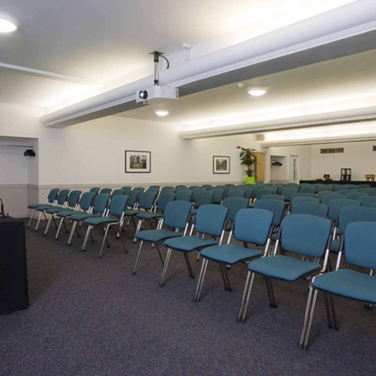 A conference room set up with rows of chairs facing a presentation area and a table with a laptop and water.