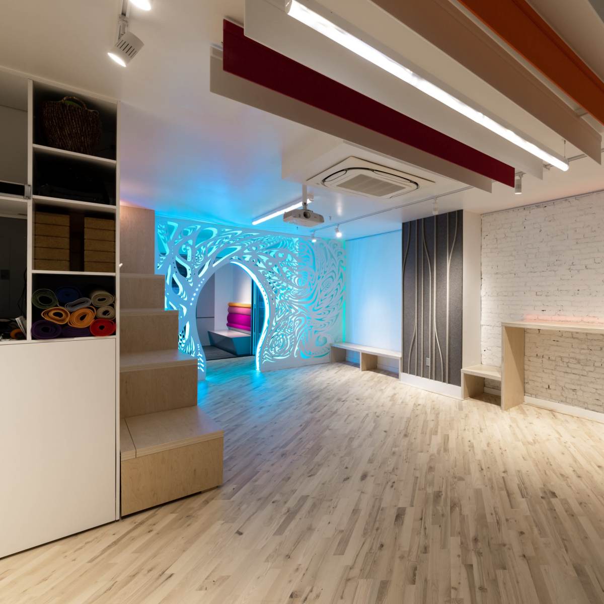 A modern, well-lit studio space featuring a textured wall, colorful accent lighting, and wooden flooring.