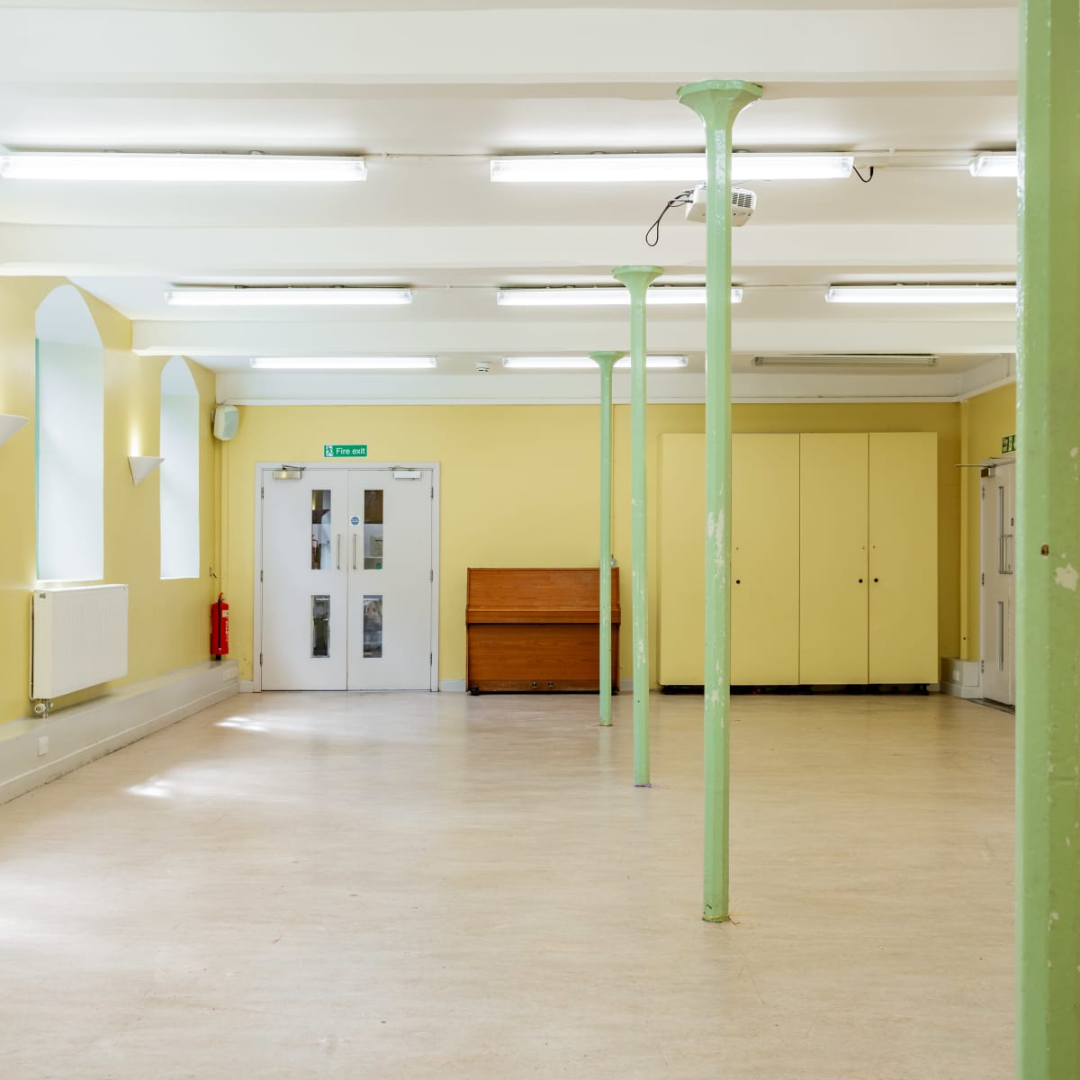 An empty room with yellow walls, fluorescent lighting, and green support columns.