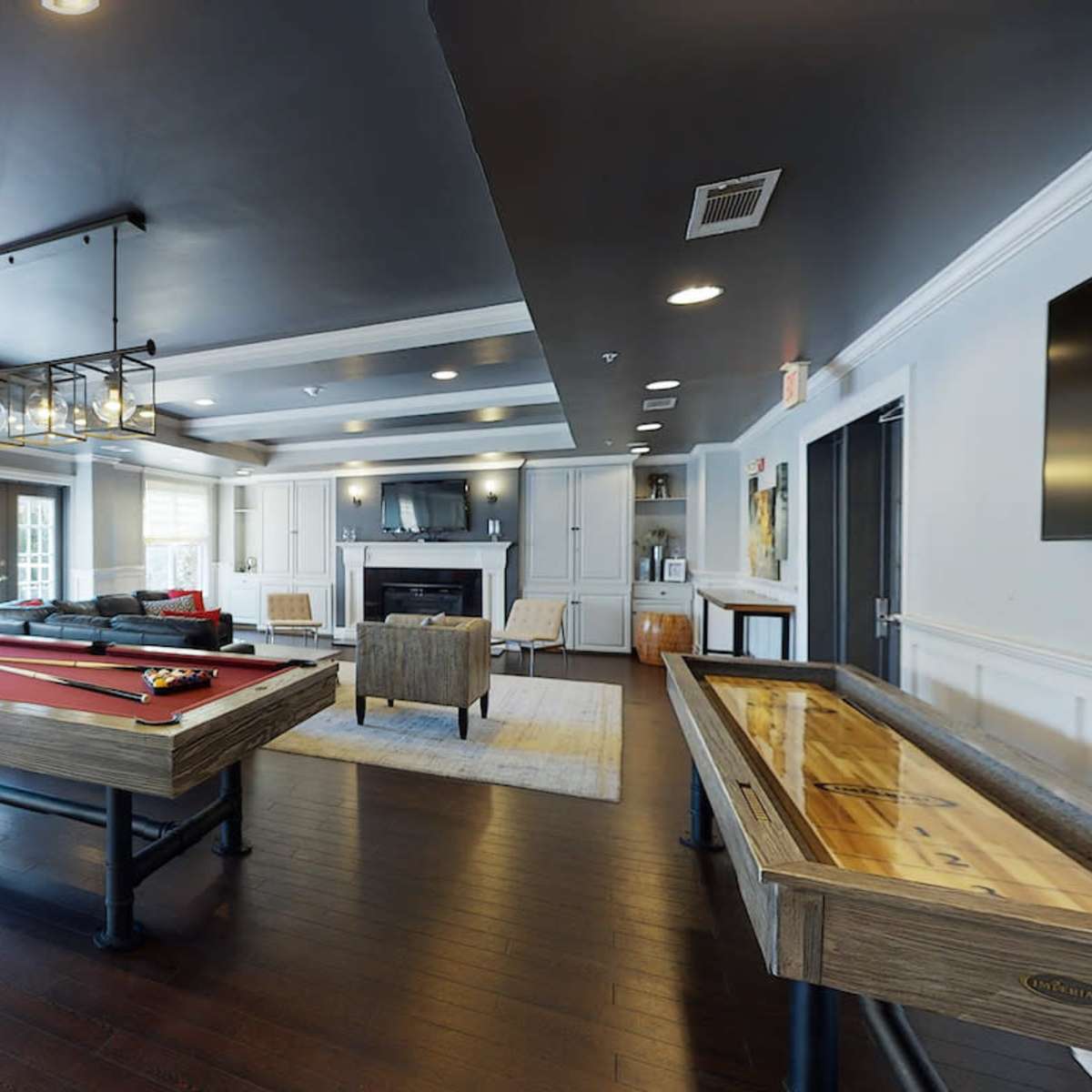 A spacious room featuring a billiards table, a shuffleboard table, a seating area, and a television against the wall.