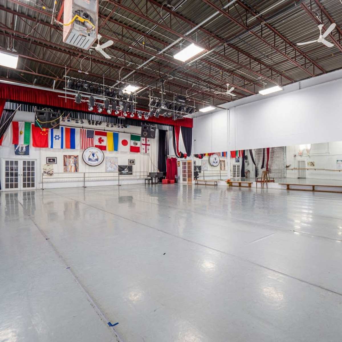 A spacious dance studio featuring a mirrored wall, ballet barre, and various flags displayed on the wall.
