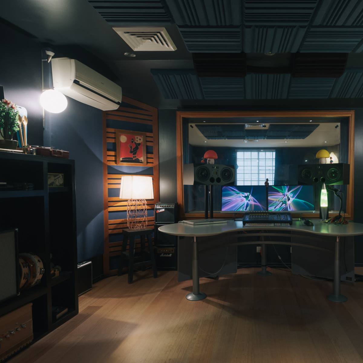 A sound recording studio features a central workstation with two monitors, flanked by audio equipment and soundproofing panels on the walls.