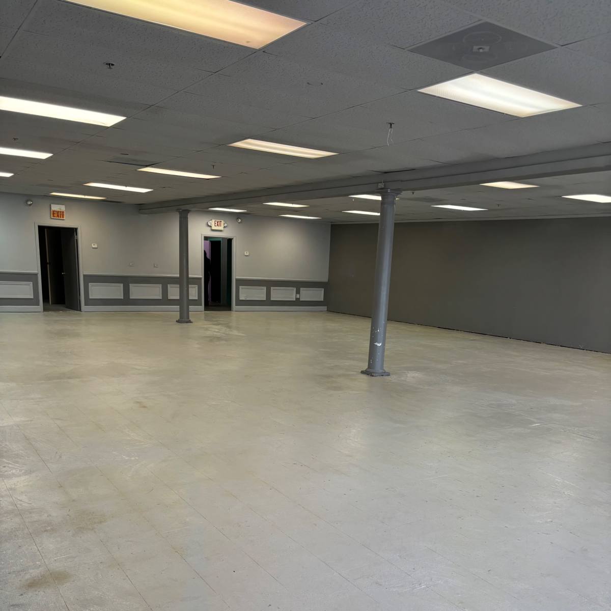 An empty room with gray walls, a light gray floor, and several doorways leading to other spaces.