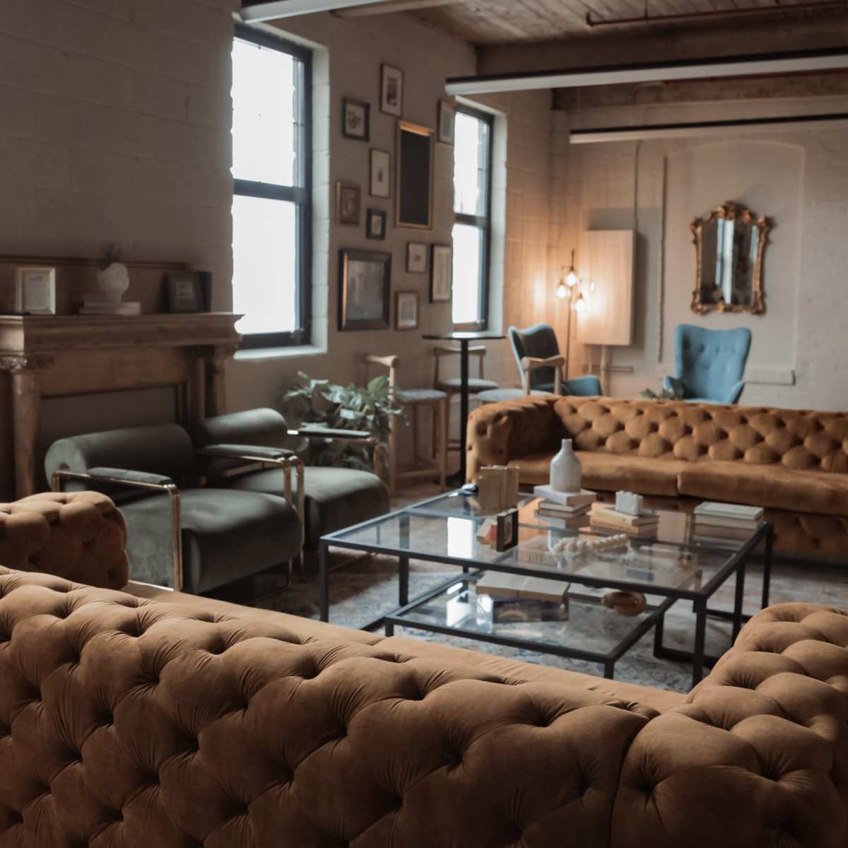 A spacious living room featuring tufted yellow sofas, a glass coffee table, and various framed artworks on the walls.