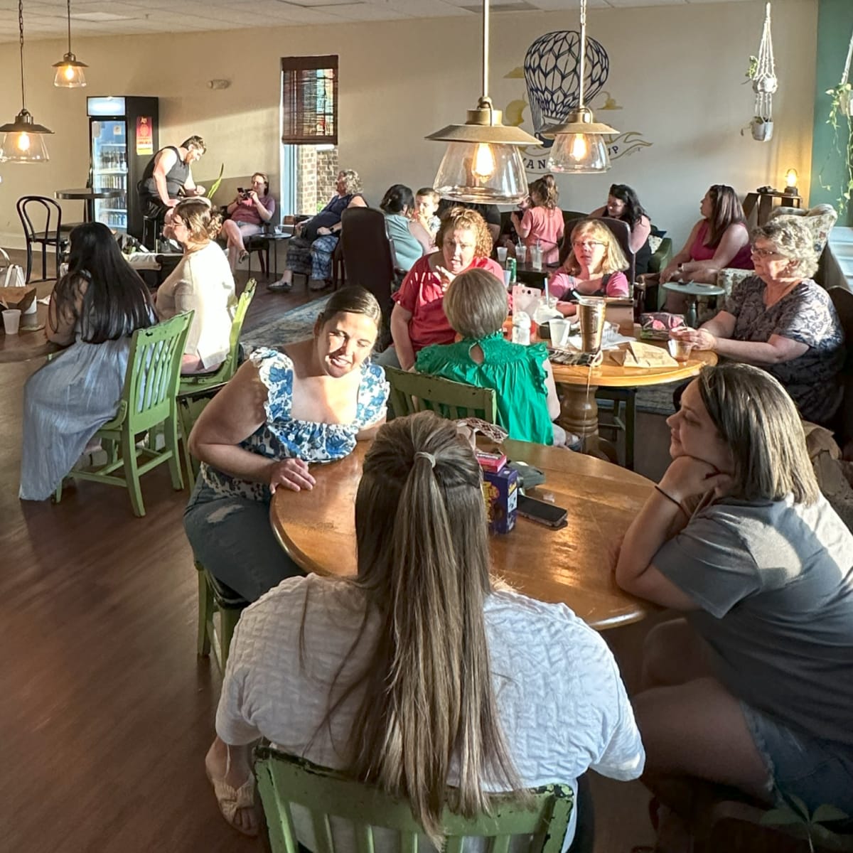 A busy café filled with patrons sitting at wooden tables, engaged in conversation and enjoying their drinks.