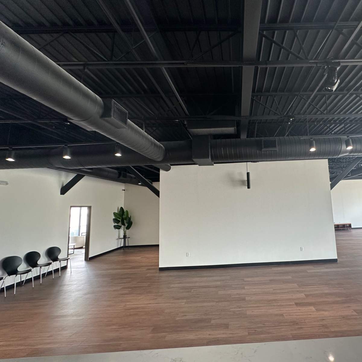 A spacious, modern interior with dark beams, hardwood flooring, and minimal furniture.