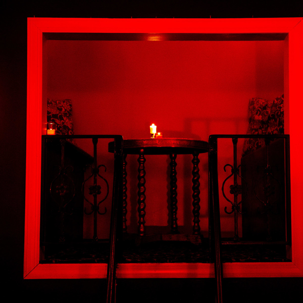 A dimly lit room features a table with a candle, illuminated by a red glow from a surrounding frame.