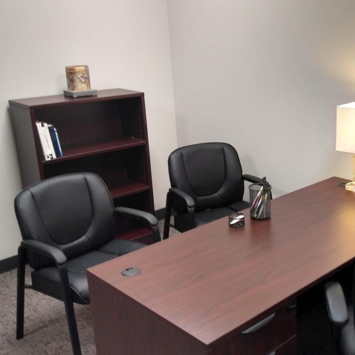 A minimalistic office space with a wooden desk, a lamp, a phone, and two black chairs arranged around a small table.