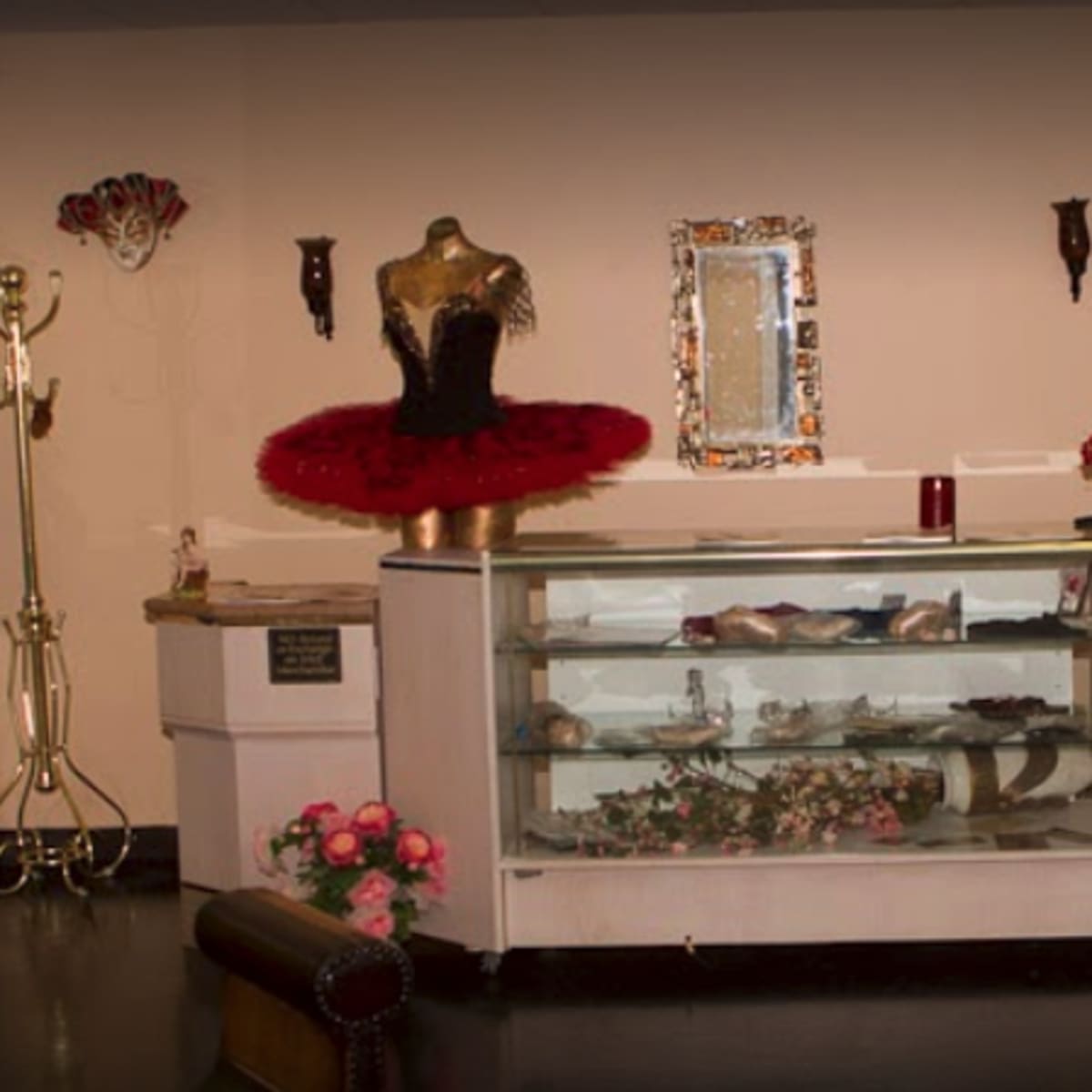 A boutique interior featuring display mannequins in ballet costumes, a showcase containing various garments, and decorative gold coat racks.