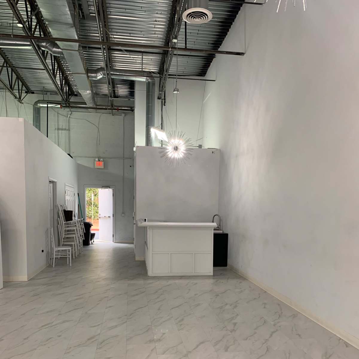 A spacious, empty interior with light-colored walls, tile flooring, and a reception area at one end.