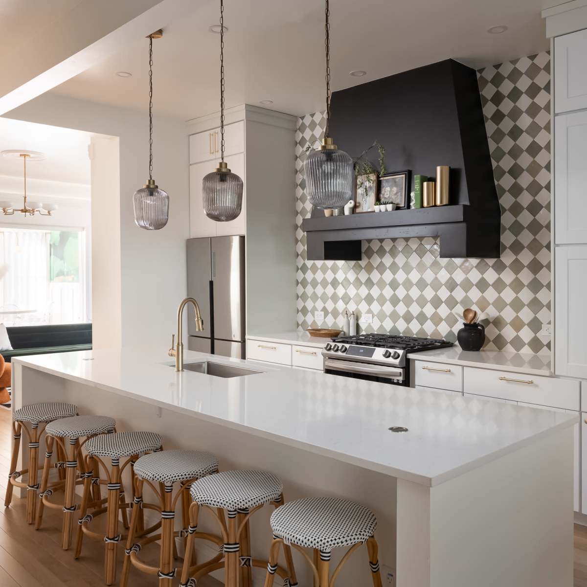 A modern kitchen features a large island with bar stools, stylish pendant lighting, and a patterned backsplash behind the stove.