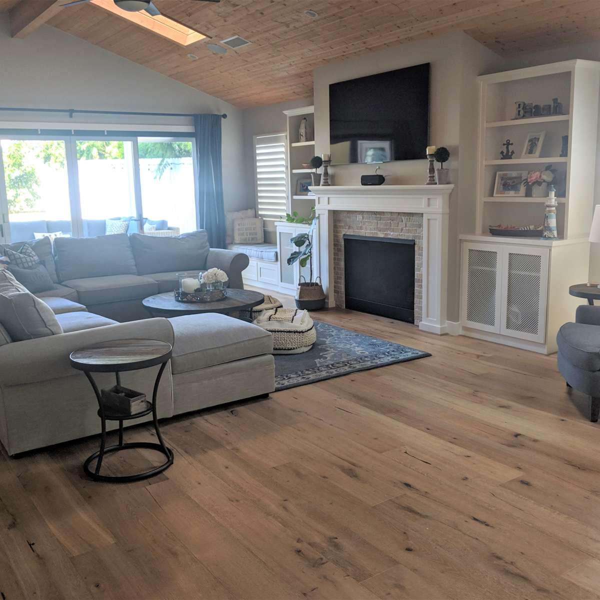 The living room features a spacious sectional sofa, a circular coffee table, a fireplace with a mantel, and large windows allowing natural light.