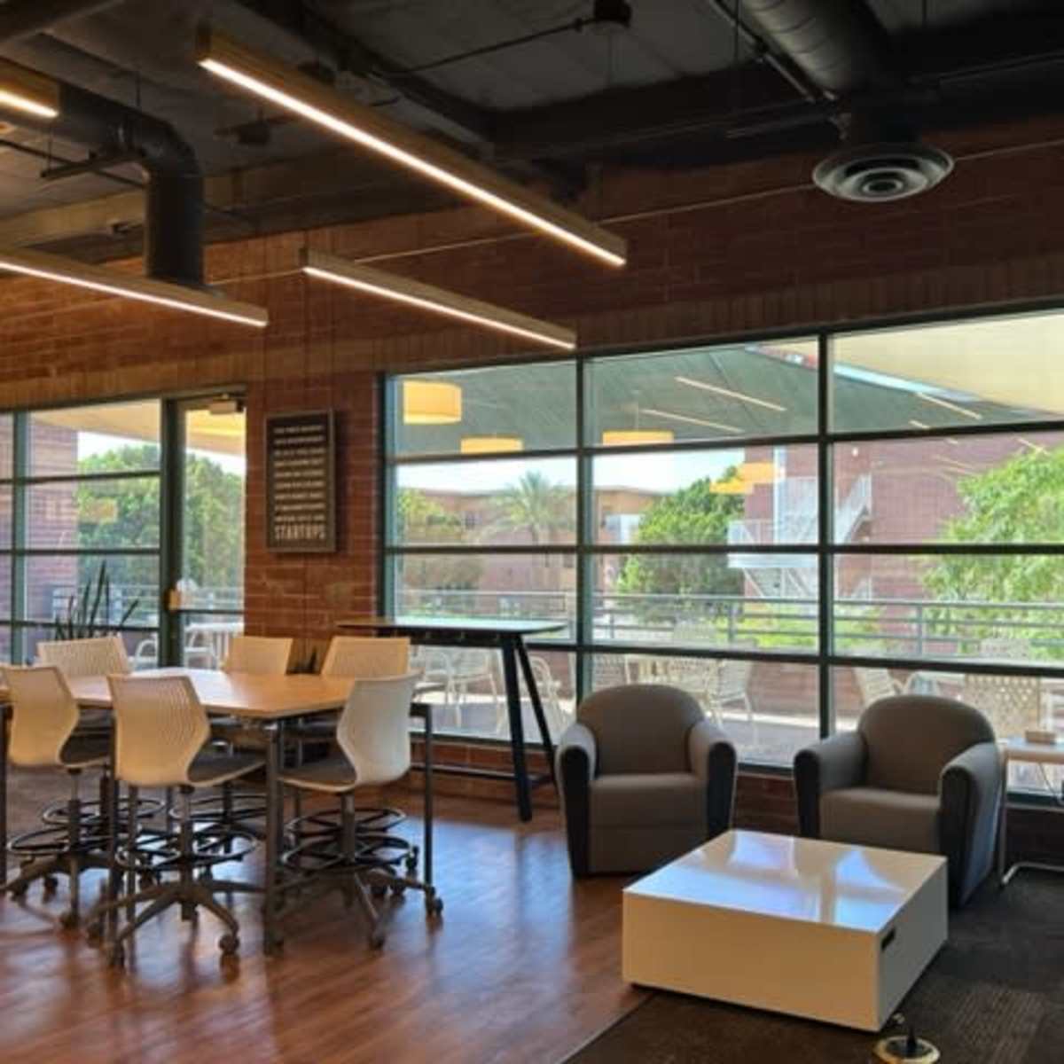 A modern seating area with two armchairs and a coffee table, adjacent to large windows providing a view of an outdoor space.