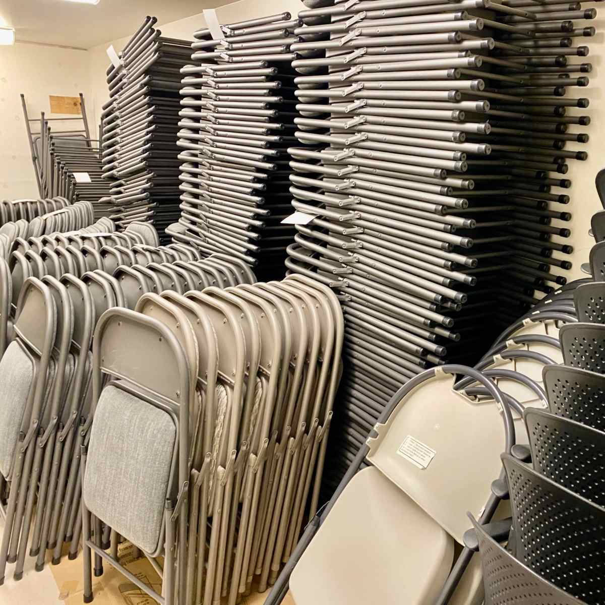 A storage room filled with neatly stacked folding chairs and black storage bins.